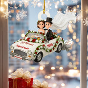 Decorative ornament of a bride and groom in a wedding car with 'Just Married' and '2025' text, against a blurred festive background.